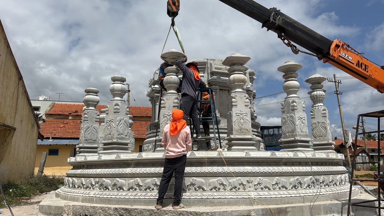 Workers guiding a crane as carved pillars are set on a circular base
