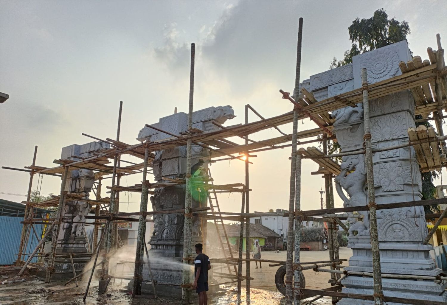 Stone gopuram under construction behind timber scaffolding at sunset