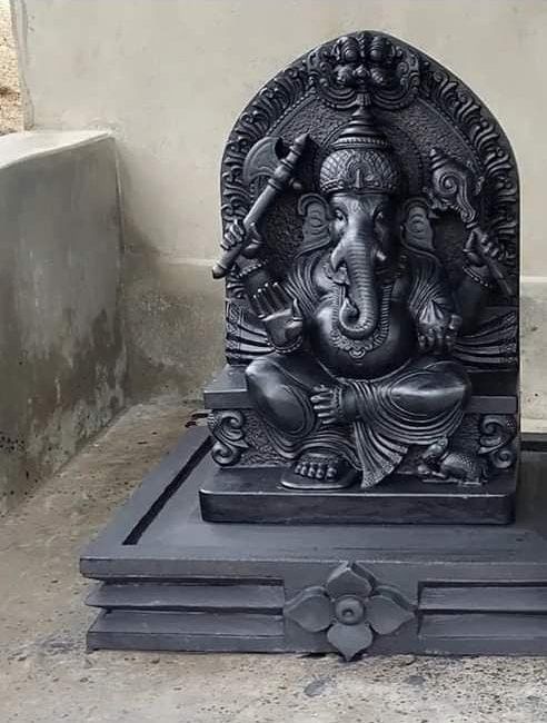 Seated black granite Ganesha murti on a carved plinth